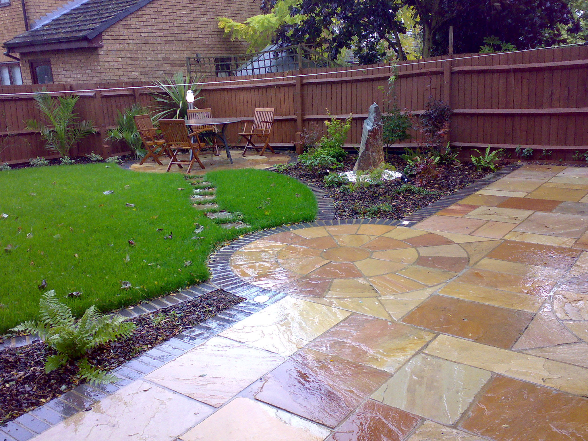 View into the garden looking at the circular seating area with glossy caramel colour new patio in the foreground